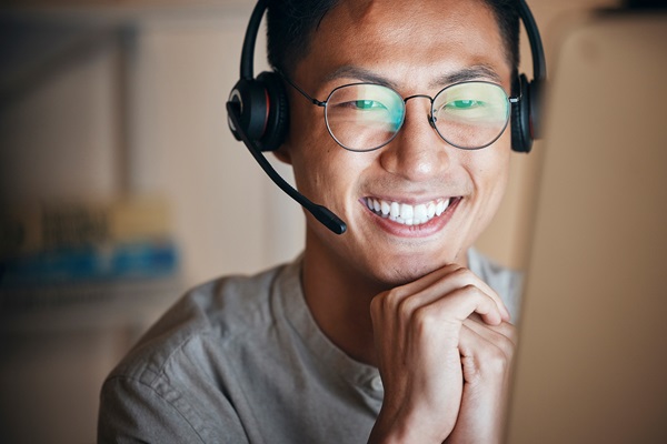 Hombre sonriente con auriculares frente al ordenador.