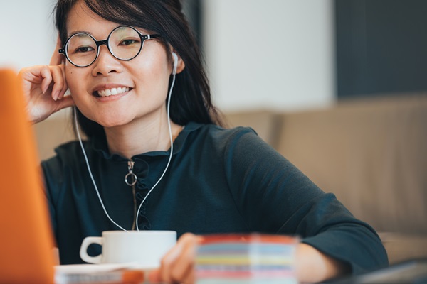 Femme souriante avec écouteurs devant un ordinateur portable.