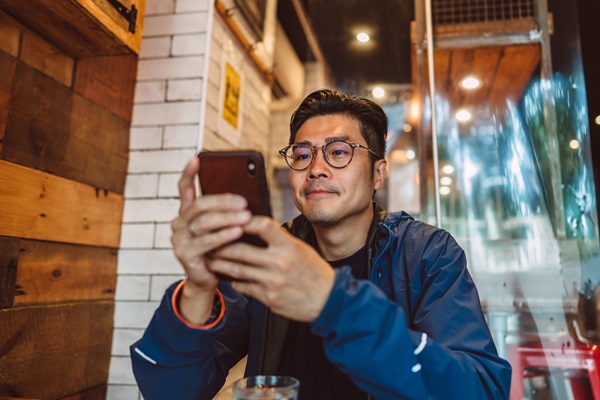 Man in café using smartphone, wooden decor background.