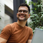 Homem sorridente com laptop, ao ar livre.